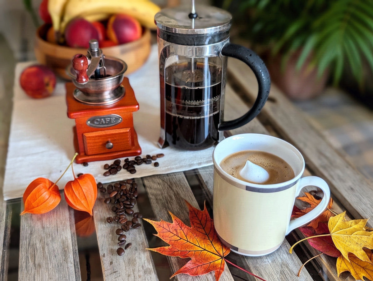 Autumn coffee still life with coffee press, mug, and scattered fall leaves on wood