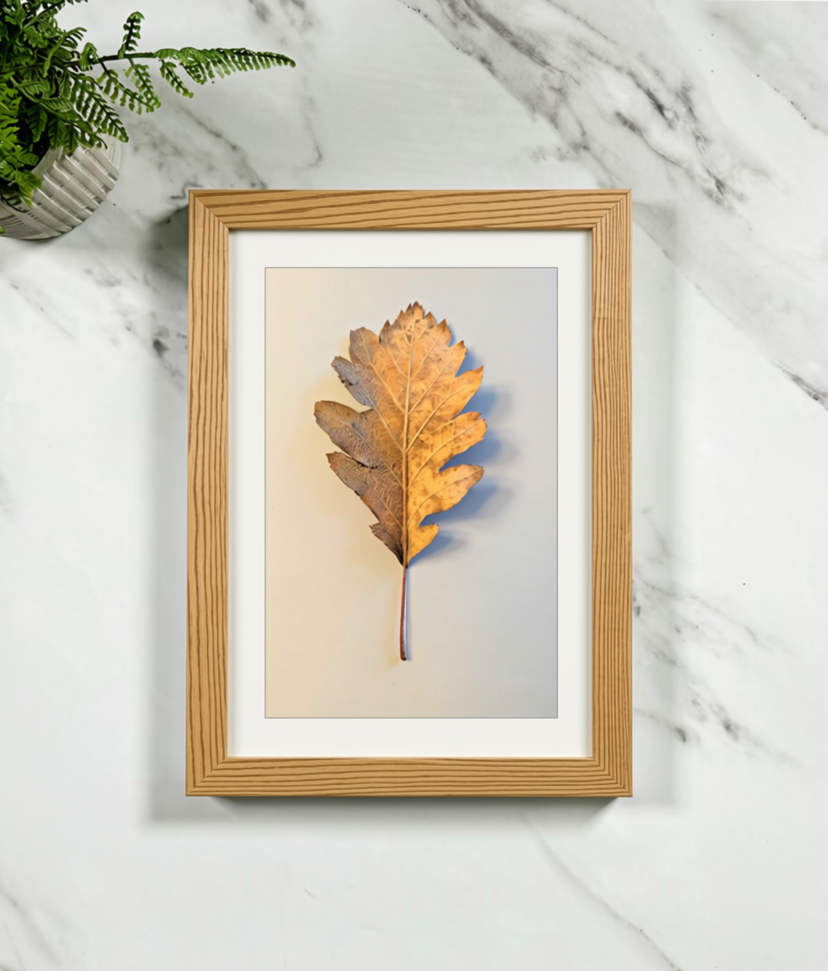 Framed botanical leaf art print with light wood frame and beige matte background